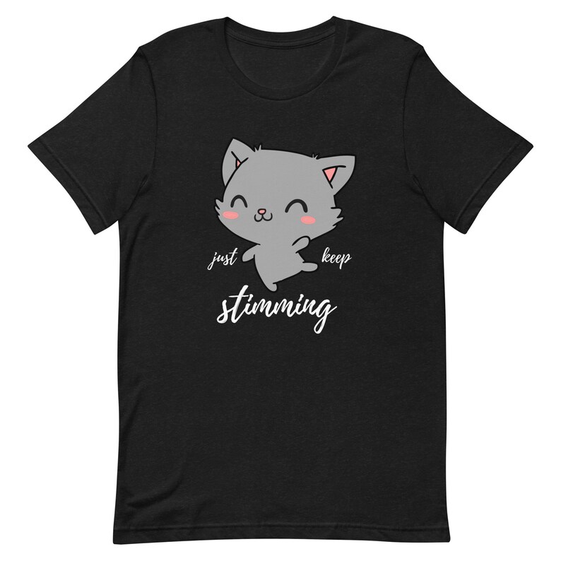 Op de afbeelding: Zwart T-shirt met een cartoon grijze kat met roze wangen en de tekst "just keep stimming" in wit.