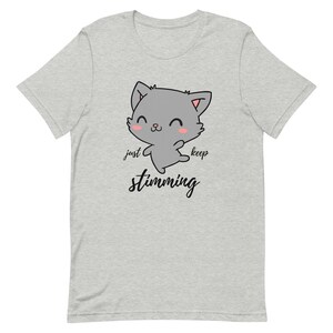 Op de afbeelding: Grijs T-shirt met een cartoonkat en de tekst "just keep stimming" in zwart.