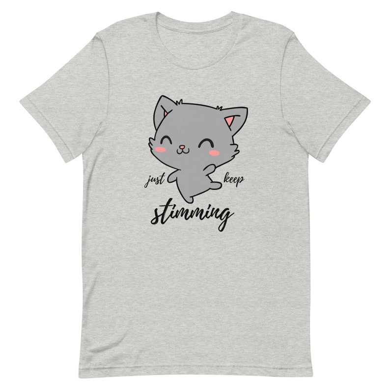 Op de afbeelding: Grijs T-shirt met een cartoonkat en de tekst "just keep stimming" in zwart.