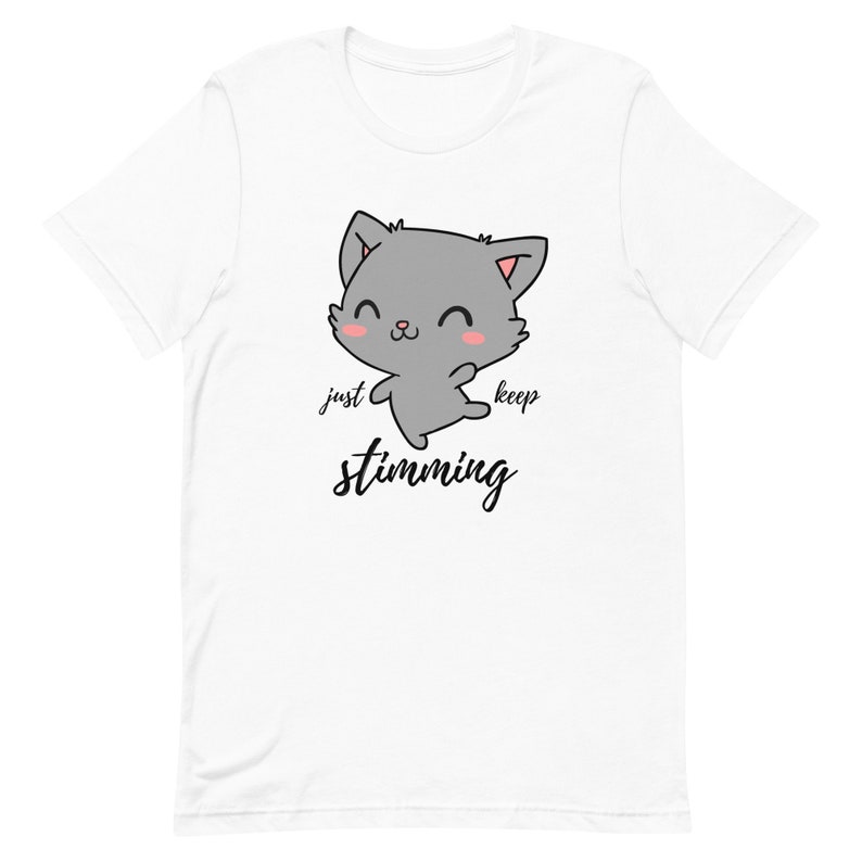 Op de afbeelding: Wit T-shirt met een cartoon grijze kat met roze wangen en de tekst "just keep stimming" in zwart.