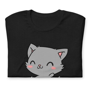 Op de afbeelding: Zwart T-shirt met een schattige cartoon grijze kat met roze wangen en een witte omtrek. De kat glimlacht en heeft zijn poot opgeheven.