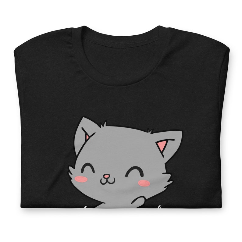 Op de afbeelding: Zwart T-shirt met een schattige cartoon grijze kat met roze wangen en een witte omtrek. De kat glimlacht en heeft zijn poot opgeheven.