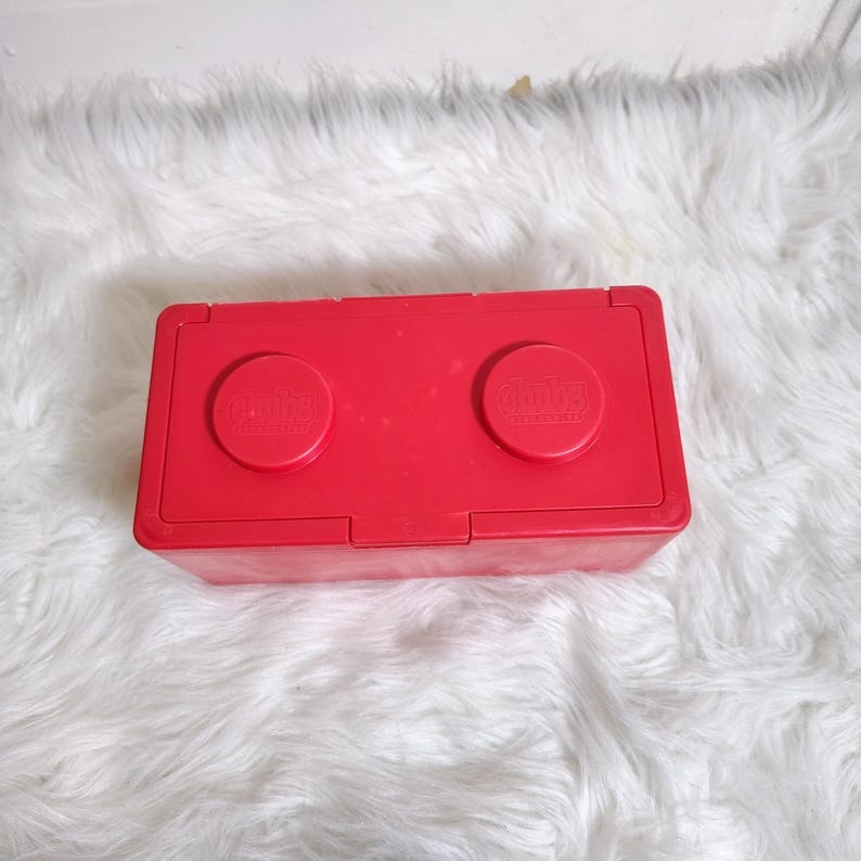 K&ouml;nnte beinhalten: Eine leuchtend rote, rechteckige Aufbewahrungsbox mit zwei runden Deckeln, auf denen jeweils das "Chitty"-Logo zu sehen ist. Der Beh&auml;lter besteht aus Kunststoff und hat einen Klappdeckel. Auf flauschigem, wei&szlig;em Hintergrund.