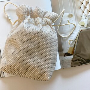 May include: A white beaded drawstring bag with a white cord handle. The bag is sitting on a magazine.