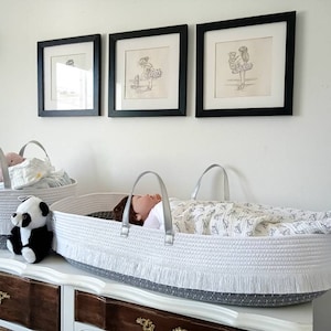 May include: Two white and gray woven baskets with fringe trim. One basket is filled with baby supplies and the other has a baby doll inside. A black and white panda plush toy sits on the dresser next to the baskets.