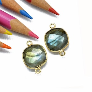 May include: Two gold-toned metal connector charms with a square-shaped labradorite gemstone in the center. The gemstones are a dark gray with iridescent blue and green hues.