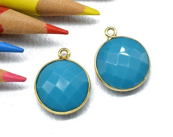 May include: Two turquoise blue gemstone pendants with gold settings. The gemstones are faceted and have a round shape.