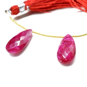 May include: Two faceted pink gemstone drops strung on a gold wire with a red tassel.