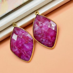 May include: Two pink gemstone pendants with gold settings. The gemstones are faceted and have a marbled appearance.