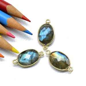 May include: Three oval-shaped labradorite gemstone connector charms with gold-toned metal accents. The stones are a dark blue-grey with iridescent flashes of color.