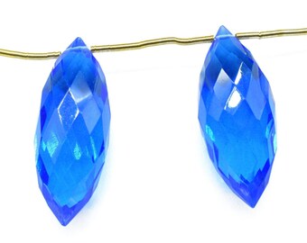 May include: Two bright blue faceted teardrop-shaped crystal beads strung on a gold wire.