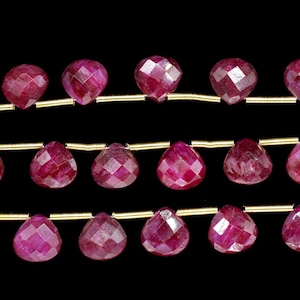 May include: A strand of ruby gemstone beads, each bead is faceted and shaped like a teardrop. The beads are strung on a gold wire.