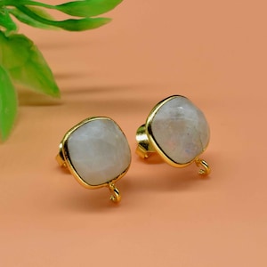 May include: A pair of gold earrings with white moonstone square-shaped stones. The earrings have a gold hook closure.