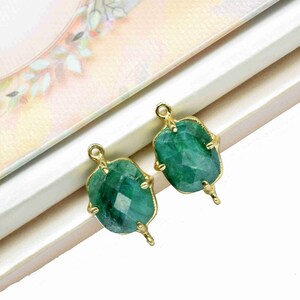 May include: Two green gemstone pendants with gold settings. The gemstones are faceted and have a rough, irregular shape. The gold settings have a delicate, ornate design.