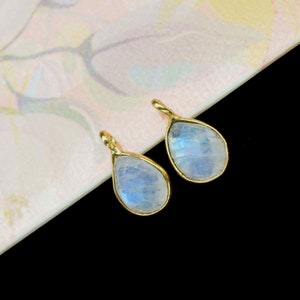 May include: Two teardrop-shaped moonstone pendants with gold settings. The stones are iridescent and have a milky white colour.