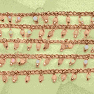 May include: A close-up of a gold chain with small, white beads hanging from it. The chain is layered on a green background.