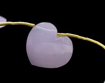 May include: A close-up of a light pink heart-shaped bead strung on a gold wire. The bead is smooth and polished.