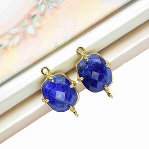 May include: Two gold-toned pendant charms with blue gemstone accents. The gemstones are faceted and have a slightly oval shape.