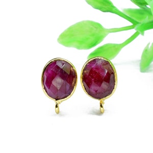 May include: A pair of gold-toned earrings with red gemstone accents. The earrings have a simple, elegant design and are perfect for everyday wear.
