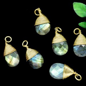 May include: Six gold-wrapped labradorite gemstone pendants with a teardrop shape. The pendants are on a black background.
