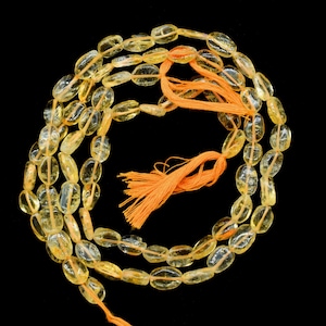 Könnte beinhalten: Eine Kette aus ovalen, durchscheinenden gelben Citrinperlen mit einem Quaste aus orangefarbenem Garn.