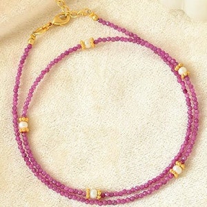 May include: A delicate double-strand necklace with small pink beads and gold accents. The necklace features small white pearls interspersed throughout the beads.