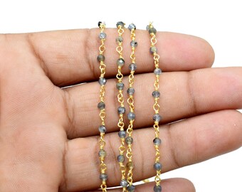 May include: A strand of gold chain with small, dark gray beads. The chain is laid out on a hand, showing the length and detail of the beads.