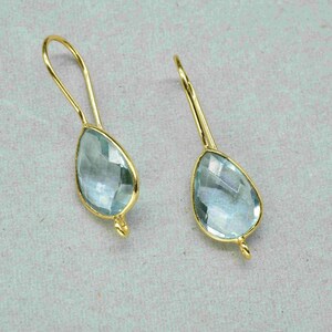 May include: A pair of gold dangle earrings with light blue teardrop-shaped gemstones.