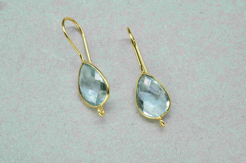 May include: A pair of gold dangle earrings with light blue teardrop-shaped gemstones.