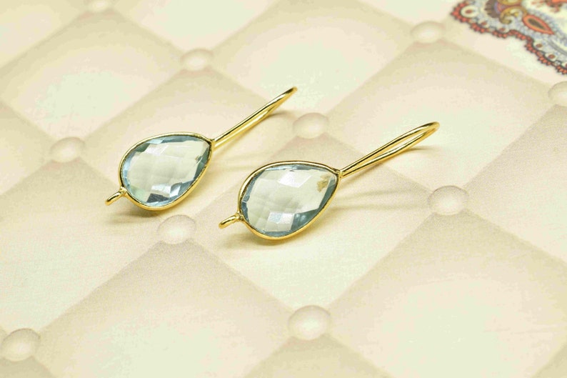 May include: A pair of gold earrings with light blue teardrop-shaped gemstones.