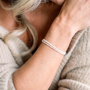 May include: A delicate double strand bracelet made of small white pearls. The bracelet is worn on a person's wrist.