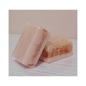 May include: Two bars of soap wrapped in clear plastic. One bar is a light brown color and has a loofah texture. The other bar is a light pink color and has a smooth texture.