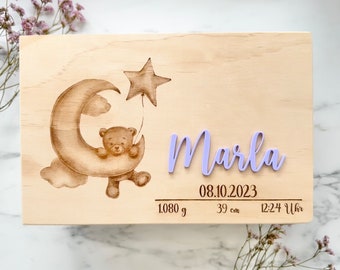 May include: A wooden keepsake box with a laser-engraved design of a teddy bear sitting on a crescent moon holding a star. The box is personalized with the name "Marla" in purple lettering and includes the birth details: 08.10.2023, 1080 g, 39 cm, 12:24 Uhr.