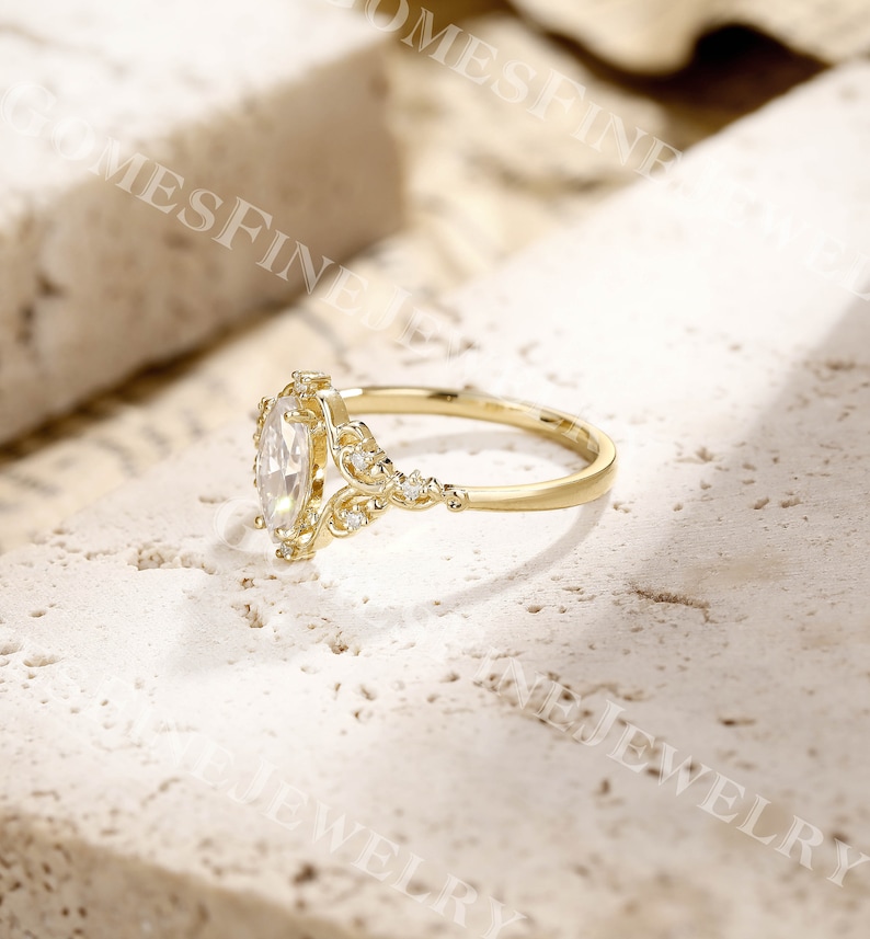 Op de afbeelding: Een gouden verlovingsring met een marquise-geslepen diamant als middensteen. De ring heeft ingewikkelde filigraan details en kleine accentdiamanten. De band is een eenvoudig, gepolijst goud. De ring staat tegen een neutrale achtergrond.