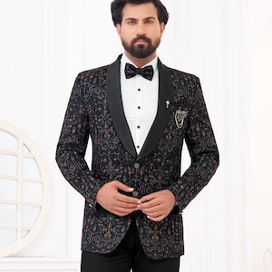 May include: A formal suit. The black blazer has a patterned design in blue, red, and gold. The suit includes black trousers, a white dress shirt, and a black bow tie. A decorative pin is on the lapel. The suit is suitable for a wedding.