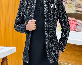 May include: Black embroidered jacket with a matching black tunic and pants. The jacket features intricate silver detailing and a mandarin collar. A white pocket square adds a contrasting touch to the formal ensemble. The outfit is suitable for special occasions.