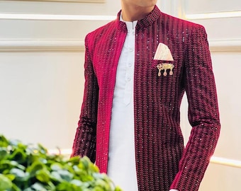 May include: A burgundy jacket with a textured pattern and a white shirt. The jacket has a contrasting panel on the left side and a decorative pin on the lapel. A white pocket square is visible.