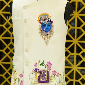 May include: Ivory-colored vest with intricate embroidery. Features a blue face design with ornate detailing and an elephant motif with a purple saddle. The text "TheIndianDarz" is visible on the left side.