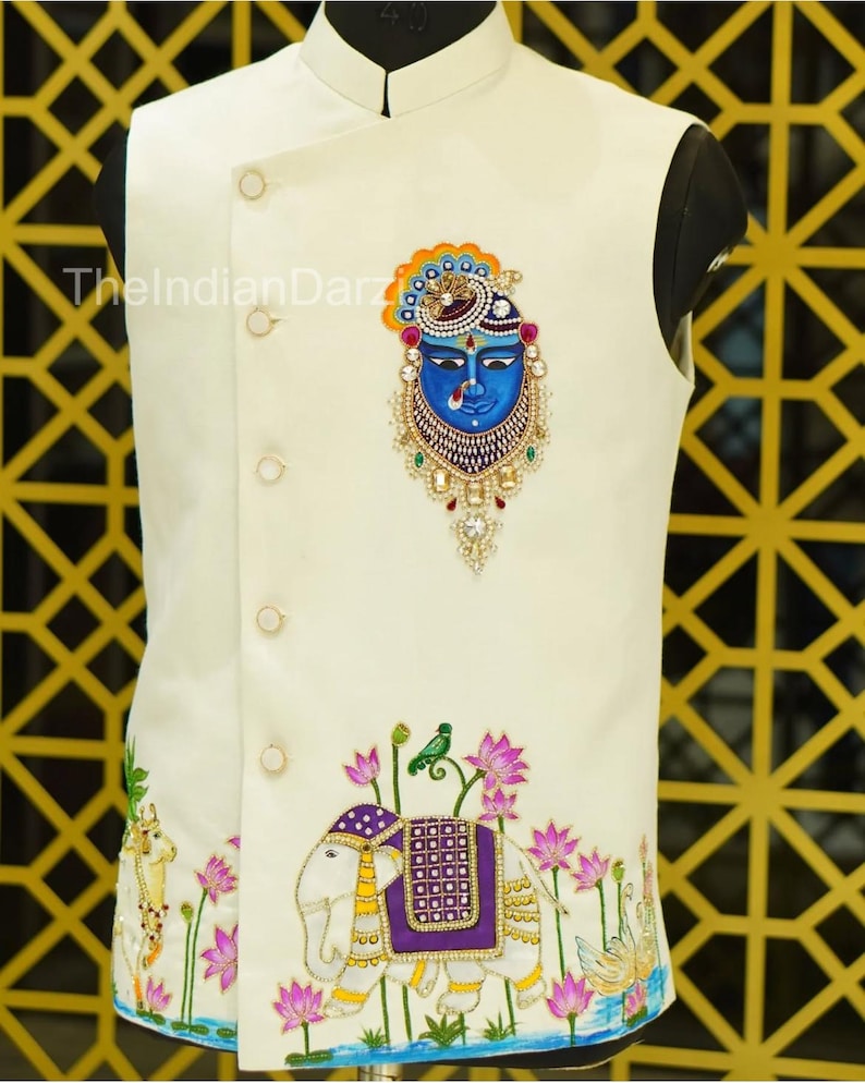 May include: Ivory-colored vest with intricate embroidery. Features a blue face design with ornate detailing and an elephant motif with a purple saddle. The text "TheIndianDarz" is visible on the left side.