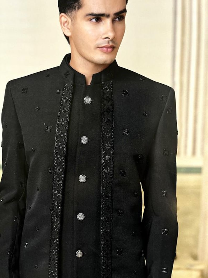 May include: A black formal jacket with a mandarin collar and decorative embellishments. The jacket features a series of silver buttons down the front and intricate detailing along the edges and down the front. The fabric has a subtle sheen, adding to its formal appearance.