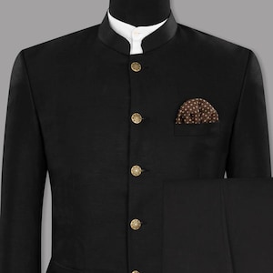 May include: A black suit with a mandarin collar, gold buttons, and a pocket square with a brown and white pattern. The suit is displayed on a mannequin. The suit includes matching black pants.