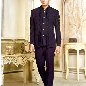 May include: A dark purple suit with a mandarin collar jacket and matching pants. The jacket features black embroidered detailing and a row of white buttons. The outfit is completed with black dress shoes, creating a formal and elegant ensemble.