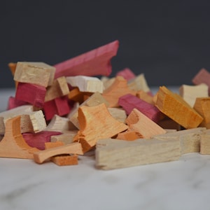 May include: A pile of wooden craft shapes in various shades of pink, orange, and beige. The shapes are irregular and have a rough, unfinished texture.