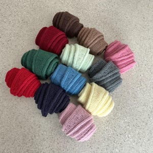 Pode incluir: Uma coleção de gorros de malha coloridos em várias tonalidades, incluindo vermelho, verde, azul e rosa. Os gorros estão dispostos em um grupo, mostrando sua textura canelada e design dobrado. Os chapéus são feitos de fio macio.