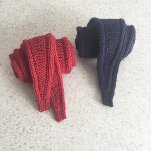 Peut inclure: Deux écharpes tricotées, l'une rouge vif et l'autre bleu marine foncé, sont présentées. Les écharpes sont pliées, mettant en valeur leur motif de tricot texturé. Ces articles sont probablement faits à la main et adaptés au froid.