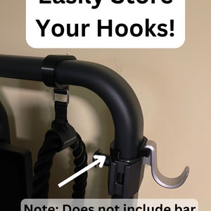 May include: A black metal hook holder with a silver hook attached to it. The holder is mounted on a black metal bar. The text "Easily Store Your Hooks!" is written on a white rectangle above the holder. The text "Note: Does not include bar hooks, this is only the holder." is written below the holder.