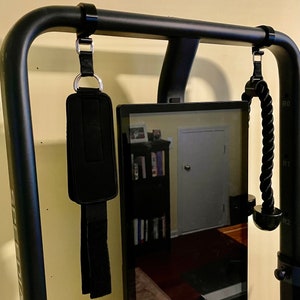 May include: Black metal frame with two black straps hanging from it. The straps have metal clips and are attached to a black padded strap and a black rope. A black screen is mounted to the frame.