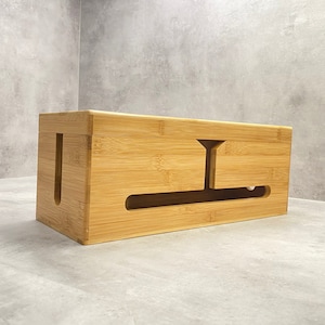 May include: A natural bamboo cable box with a rectangular shape and a cut-out for cords to pass through. The box has a light brown color and a smooth finish.