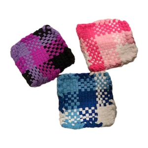 Puede incluir: Tres salvamanteles cuadrados tejidos en tonos morado, rosa y azul. Los salvamanteles están hechos de tiras de tela tejidas, cada uno con un esquema de color diferente. Los salvamanteles están diseñados para proteger las superficies del calor.