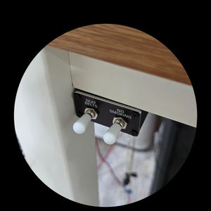 May include: A black panel with two white toggle switches. The panel is labeled "SEAT BELTS" and "NO SMOKING". The panel is mounted under a wooden surface.
